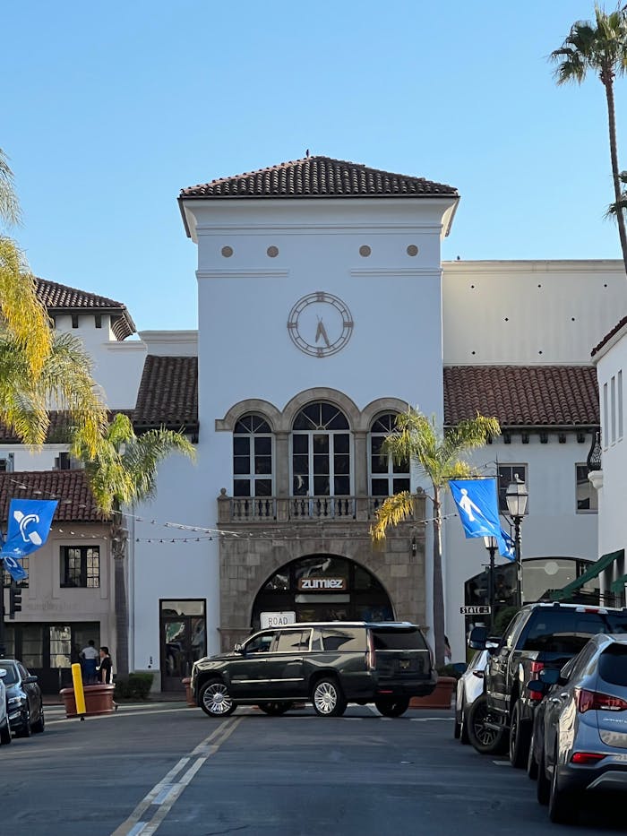 Street view of Spanish Colonial style architecture in Santa Barbara, CA, featuring parked cars and palm trees.