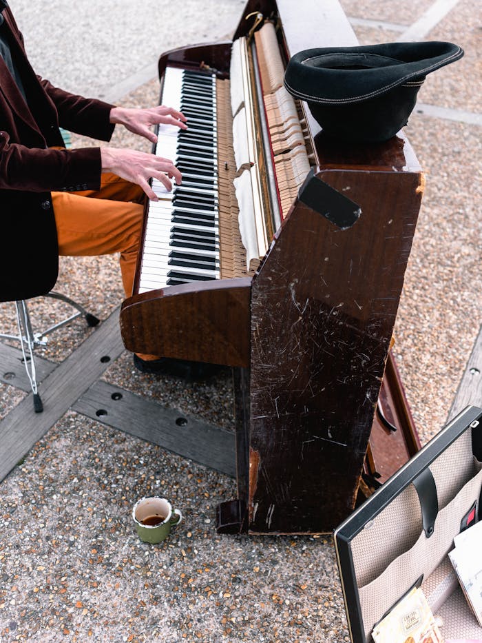 Street musician playing a piano outdoors in Étretat, France with a tip hat on the piano.