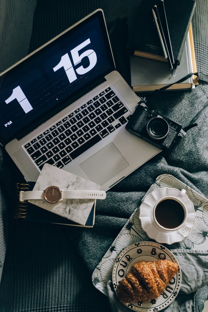 Cozy workspace setup featuring a laptop, camera, coffee, and croissant for a productive home office vibe.