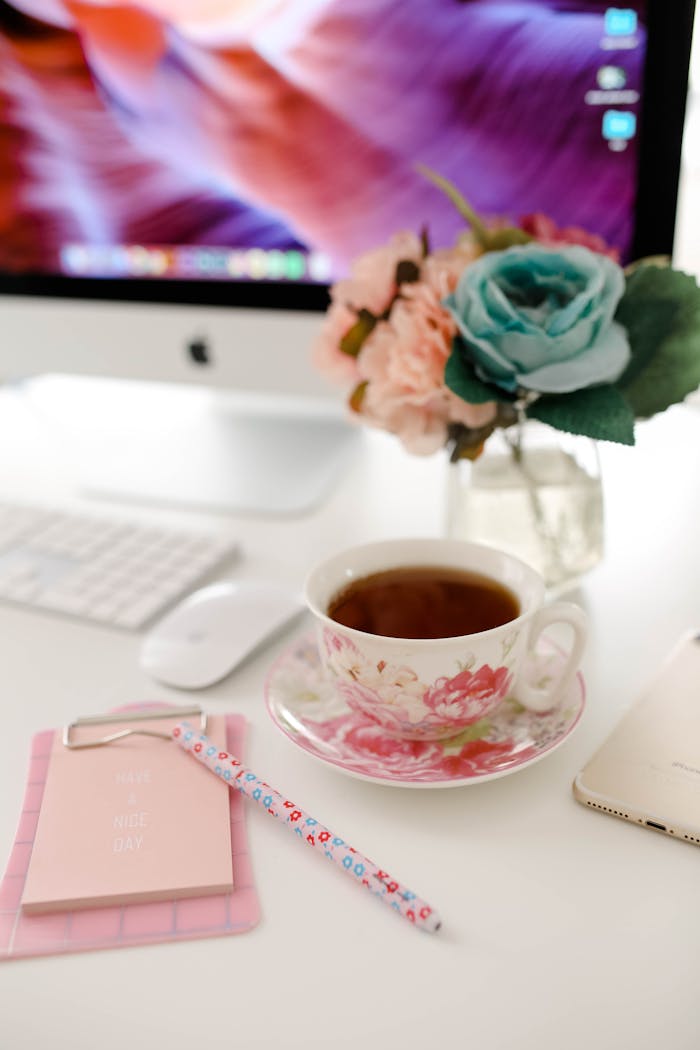 A stylish workspace featuring a tea cup, flowers, and a computer on a desk.